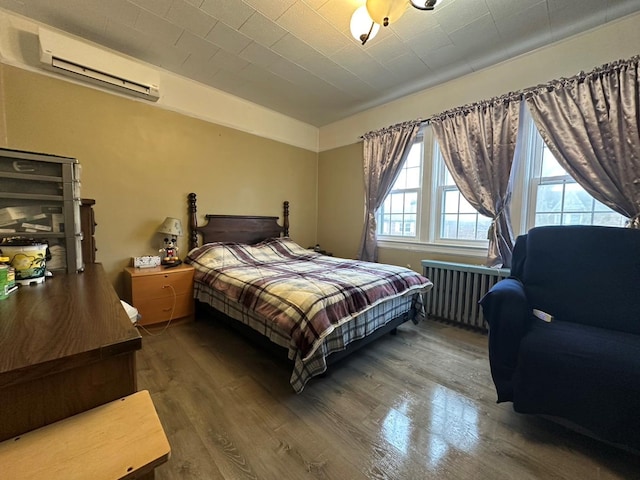 bedroom with a wall mounted air conditioner, radiator heating unit, and hardwood / wood-style floors