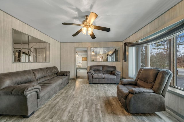 living room with hardwood / wood-style floors, ceiling fan, and wood walls