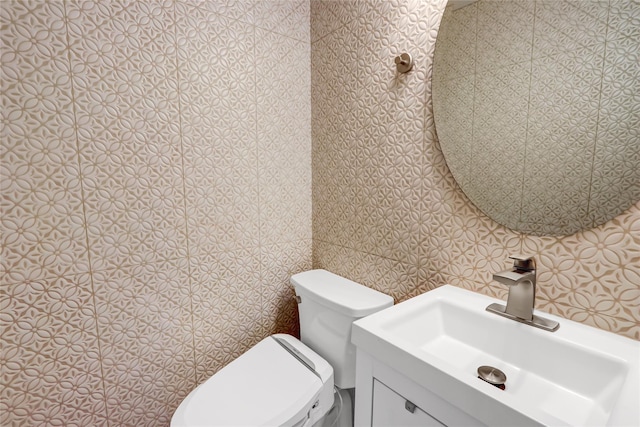 half bath featuring toilet, wallpapered walls, and vanity