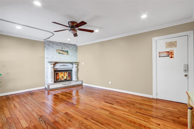 unfurnished living room featuring a ceiling fan, wood finished floors, crown molding, and a stone fireplace