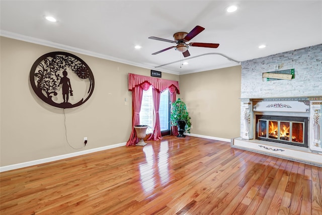 unfurnished living room with crown molding, light wood-style floors, a ceiling fan, a stone fireplace, and baseboards