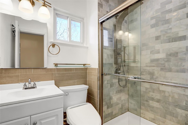 bathroom featuring toilet, a stall shower, vanity, and tile walls