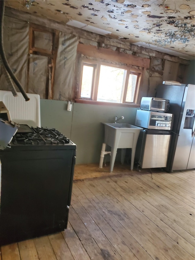 kitchen with black gas stove, stainless steel fridge, and light hardwood / wood-style floors