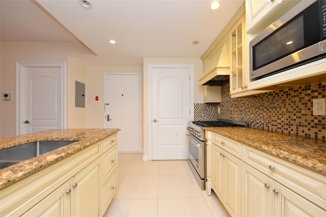 kitchen featuring appliances with stainless steel finishes, backsplash, premium range hood, light tile patterned floors, and electric panel