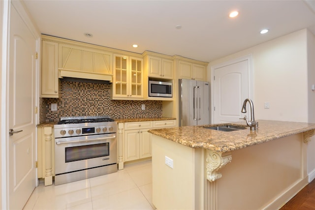 kitchen featuring high quality appliances, a kitchen island with sink, sink, cream cabinetry, and custom range hood