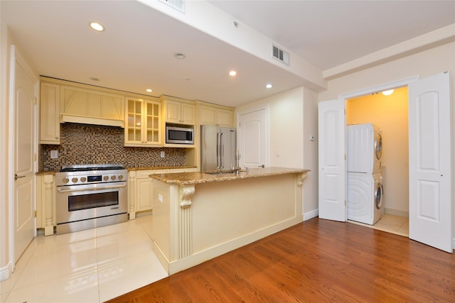 kitchen with light stone counters, cream cabinetry, a kitchen island, stacked washer and clothes dryer, and high end appliances