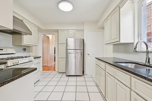 kitchen with white cabinets, dark stone counters, sink, white gas range, and stainless steel refrigerator