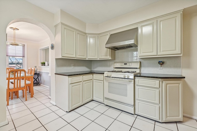 kitchen with wall chimney range hood, white range with gas cooktop, tasteful backsplash, cream cabinets, and light tile patterned flooring