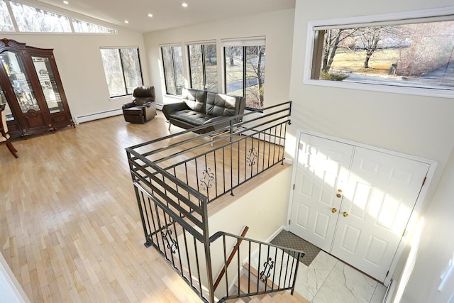 foyer featuring lofted ceiling, wood-type flooring, baseboard heating, and a wealth of natural light