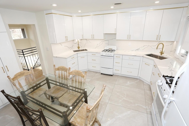 kitchen with sink, white cabinets, backsplash, and white gas range