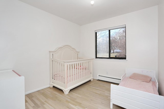 bedroom featuring light wood-type flooring, a crib, and a baseboard radiator