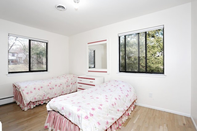 bedroom featuring baseboard heating, light hardwood / wood-style floors, and multiple windows