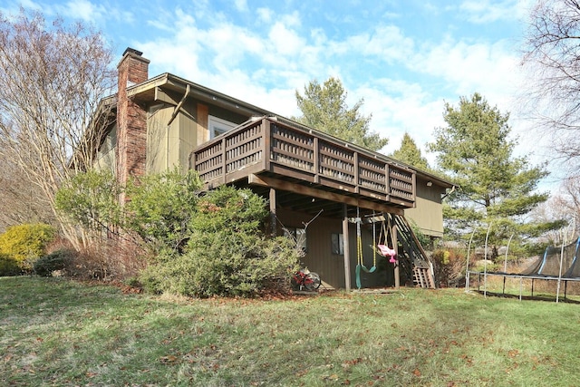 rear view of house with a yard, a trampoline, and a wooden deck