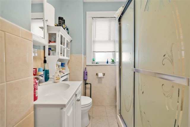 bathroom with tile patterned flooring, toilet, vanity, a shower with shower door, and tile walls