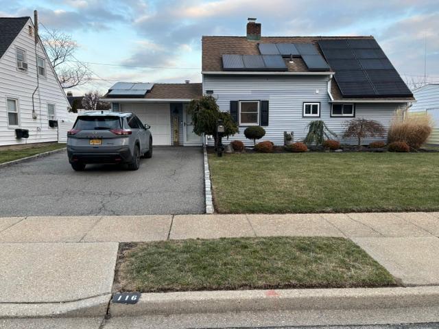 view of front facade with solar panels, a garage, and a front lawn