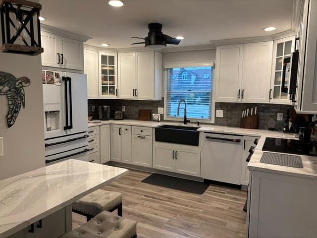 kitchen with light stone countertops, white cabinetry, stainless steel dishwasher, and sink