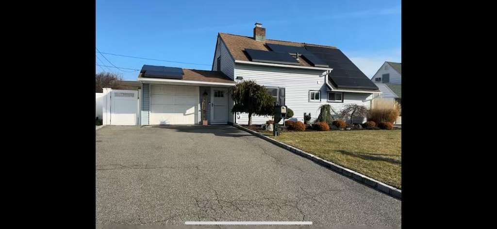 view of front of property featuring a garage, a front lawn, and solar panels