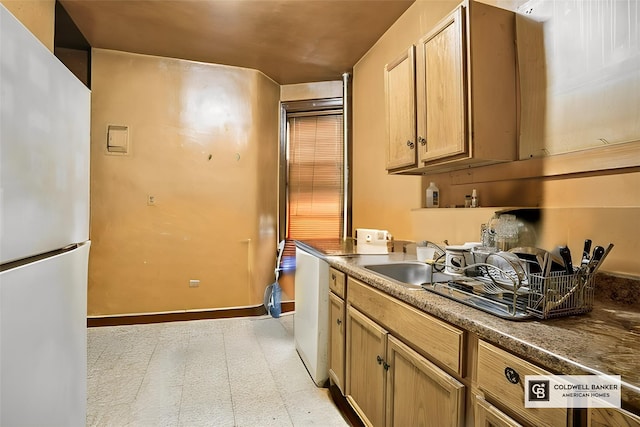 kitchen with light floors, baseboards, freestanding refrigerator, and a sink