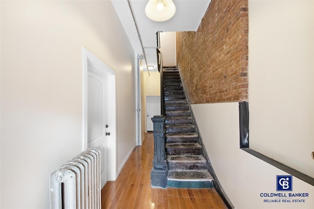 stairway with radiator, brick wall, and wood-type flooring