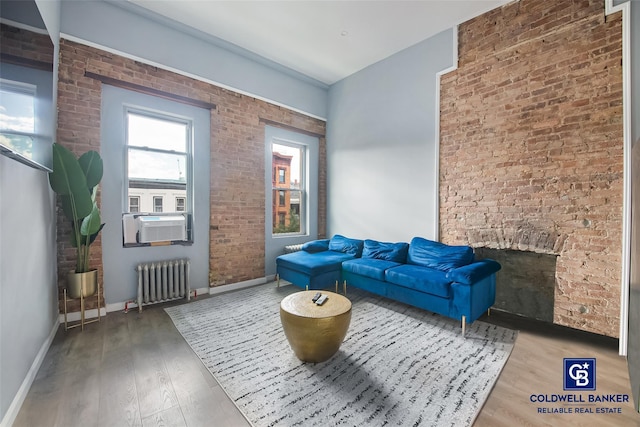 living area featuring radiator heating unit, hardwood / wood-style flooring, cooling unit, and brick wall