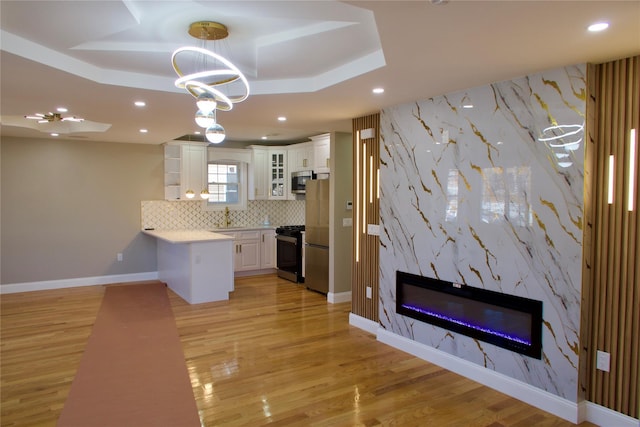 kitchen with a high end fireplace, appliances with stainless steel finishes, white cabinets, light hardwood / wood-style floors, and hanging light fixtures