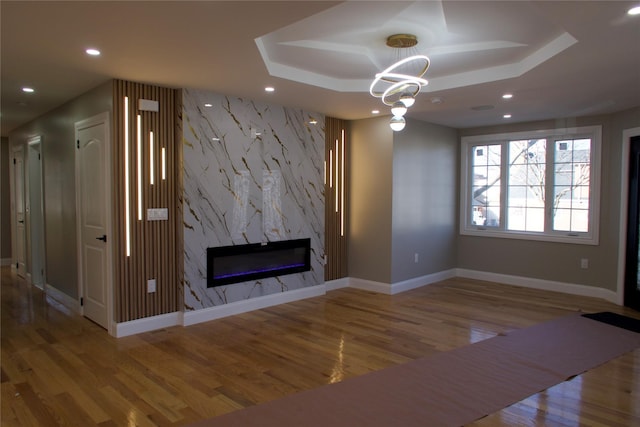 unfurnished living room featuring a tray ceiling, hardwood / wood-style flooring, a notable chandelier, and a premium fireplace