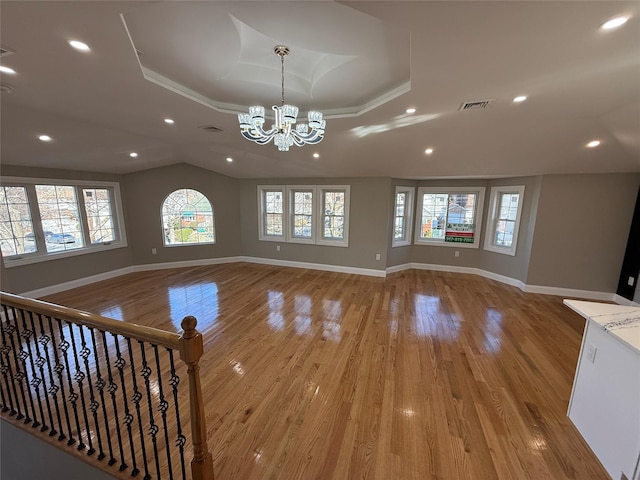 unfurnished living room with a raised ceiling, a chandelier, and light wood-type flooring