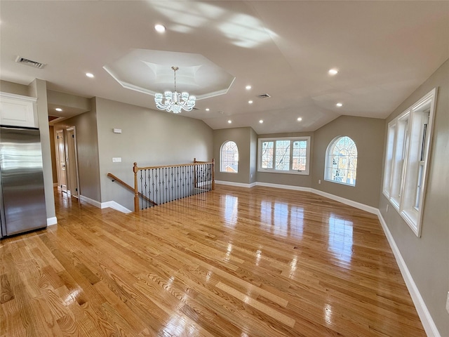 unfurnished living room featuring a raised ceiling, light hardwood / wood-style flooring, and a notable chandelier