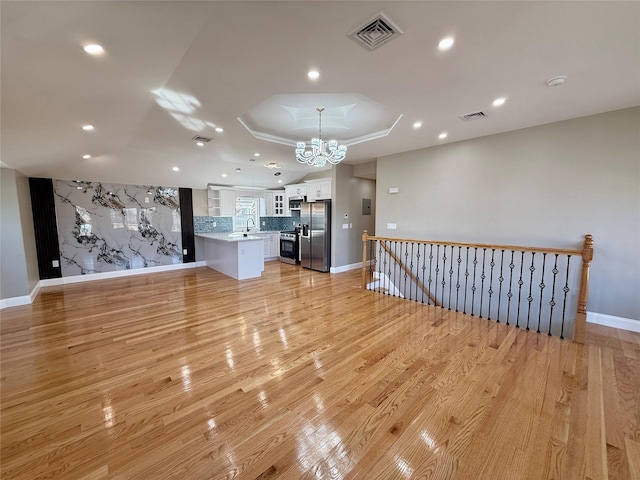 unfurnished living room featuring a raised ceiling, sink, light hardwood / wood-style flooring, and a notable chandelier