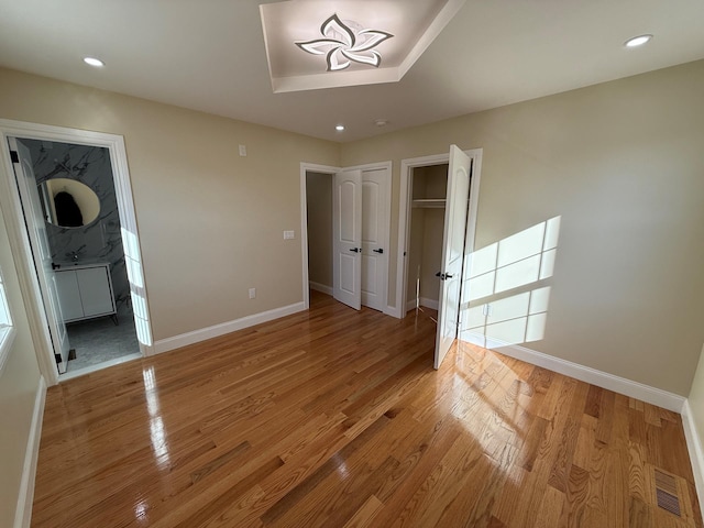 unfurnished bedroom with a tray ceiling, ensuite bath, and light hardwood / wood-style floors