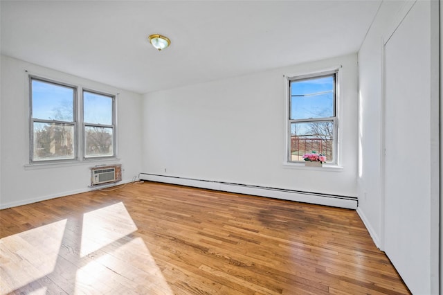 empty room with a wall mounted AC, light wood-type flooring, and a baseboard radiator