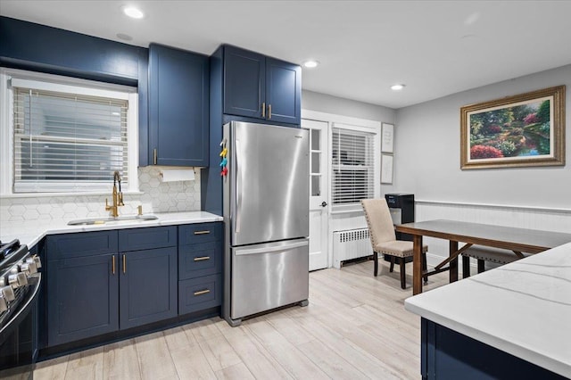 kitchen with sink, light hardwood / wood-style flooring, blue cabinetry, radiator heating unit, and stainless steel appliances