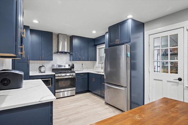 kitchen featuring blue cabinets, wall chimney range hood, backsplash, and appliances with stainless steel finishes