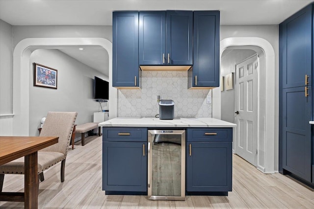 kitchen featuring tasteful backsplash, blue cabinets, beverage cooler, light stone countertops, and light hardwood / wood-style flooring