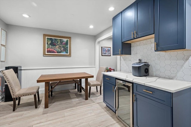 kitchen featuring blue cabinetry, beverage cooler, light stone countertops, and light wood-type flooring