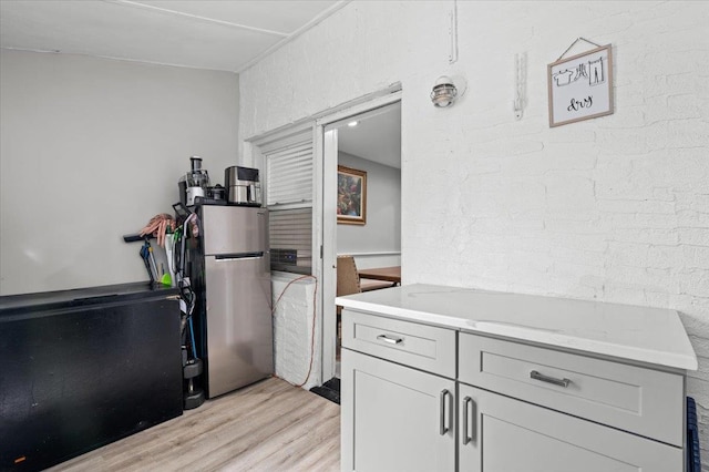 kitchen featuring light stone countertops, stainless steel refrigerator, white cabinets, and light wood-type flooring