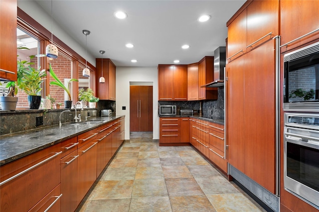 kitchen featuring pendant lighting, backsplash, dark stone counters, wall chimney range hood, and appliances with stainless steel finishes