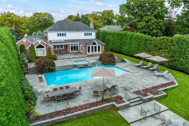 rear view of property with a swimming pool with hot tub, a patio area, and a lawn