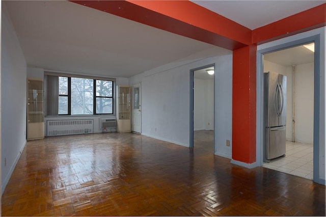 empty room featuring a wall mounted air conditioner, radiator heating unit, and light parquet flooring