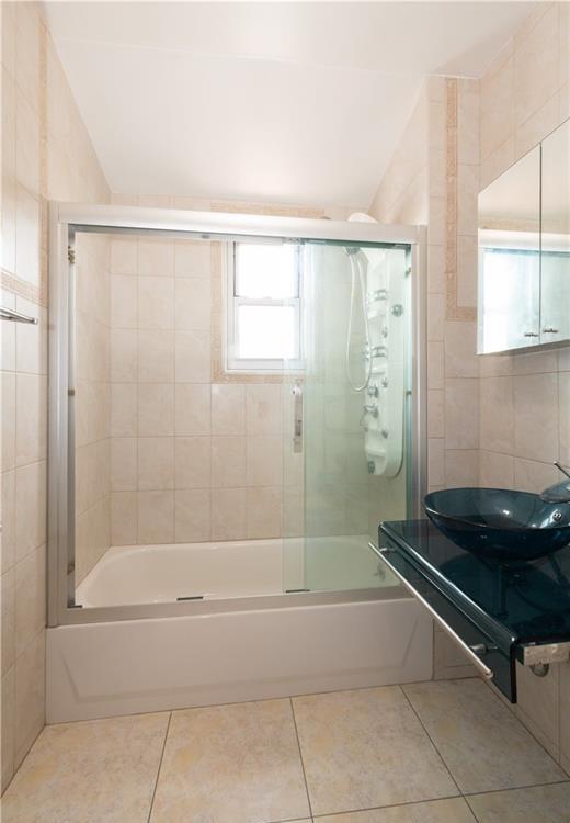 bathroom featuring tile patterned flooring, bath / shower combo with glass door, sink, and tile walls