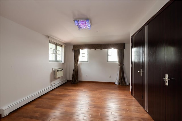 unfurnished bedroom with a wall mounted air conditioner, a closet, hardwood / wood-style floors, and a baseboard heating unit