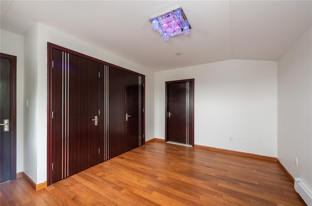 unfurnished bedroom featuring a closet, wood-type flooring, vaulted ceiling, and a baseboard heating unit