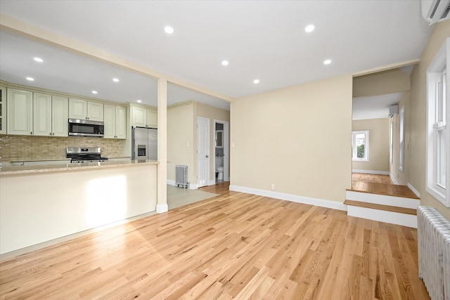 kitchen with light stone countertops, radiator heating unit, an AC wall unit, decorative backsplash, and appliances with stainless steel finishes