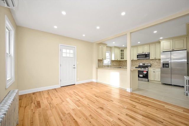 kitchen featuring backsplash, radiator, cream cabinets, light wood-type flooring, and stainless steel appliances