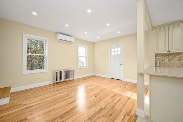 interior space with a wall mounted air conditioner, radiator, and light hardwood / wood-style flooring