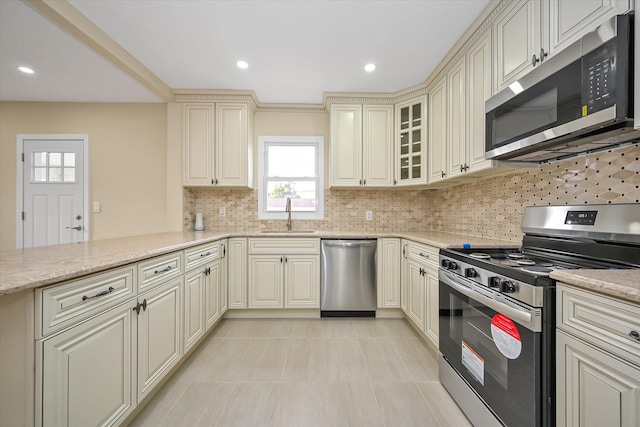 kitchen featuring appliances with stainless steel finishes, backsplash, light stone counters, sink, and cream cabinets