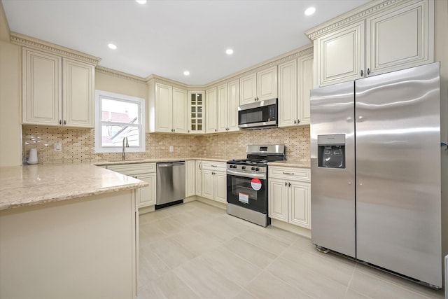 kitchen featuring sink, decorative backsplash, light stone countertops, appliances with stainless steel finishes, and cream cabinetry