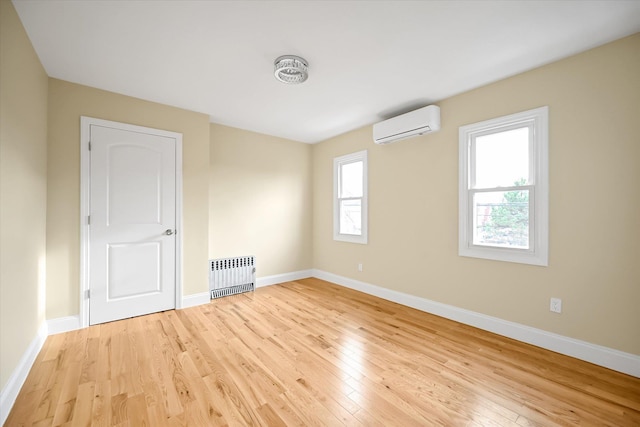 empty room with an AC wall unit, radiator heating unit, a healthy amount of sunlight, and light hardwood / wood-style floors