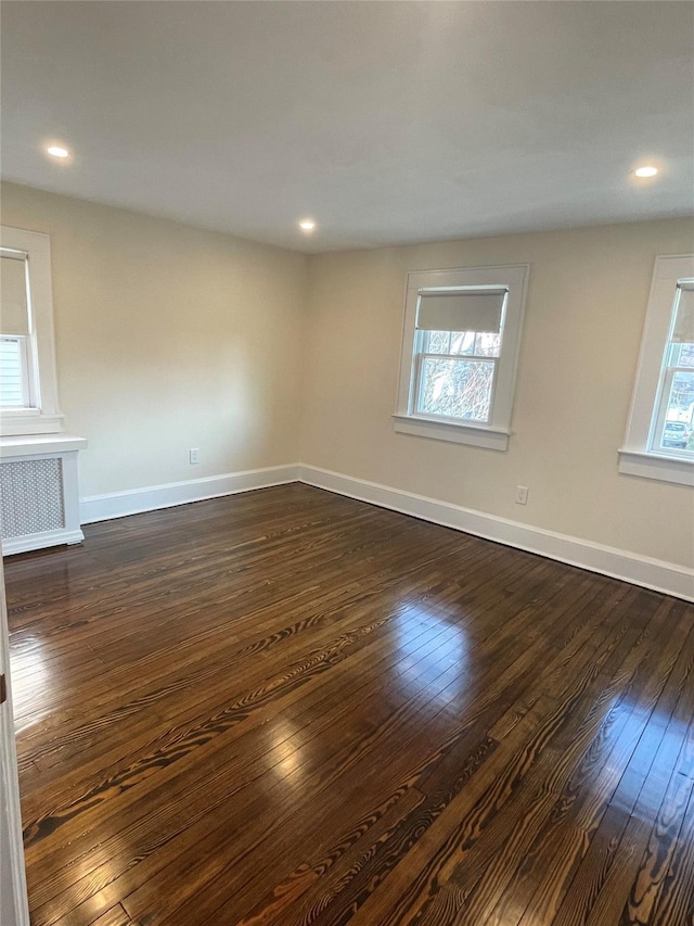 empty room featuring plenty of natural light, dark wood-type flooring, and radiator heating unit