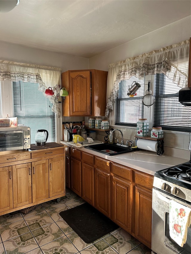 kitchen with tasteful backsplash, sink, gas range oven, and tile patterned flooring